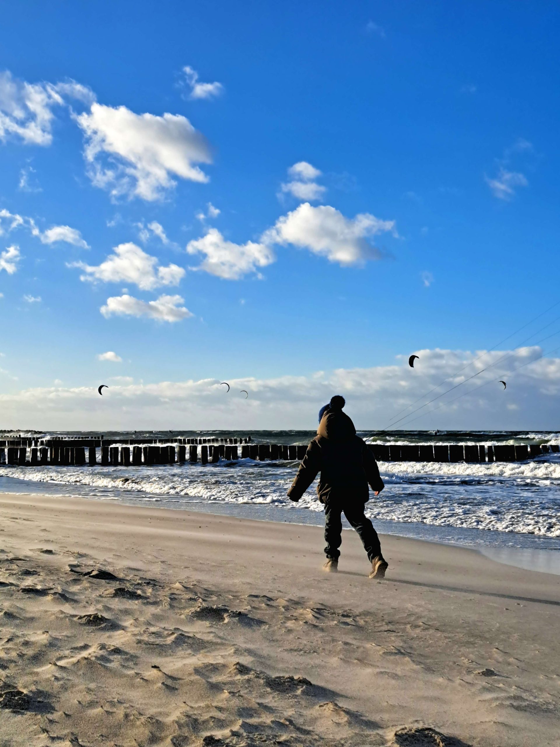 Ein Kind läuft den Ostseestrand entlang, darüber ein blauer Himmel mit vereinzelten weißen Wolken.