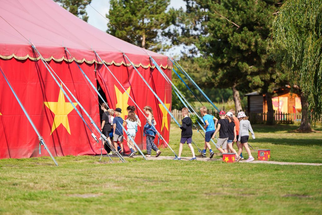 Kinder laufen in ein rotes Zirkuszelt.