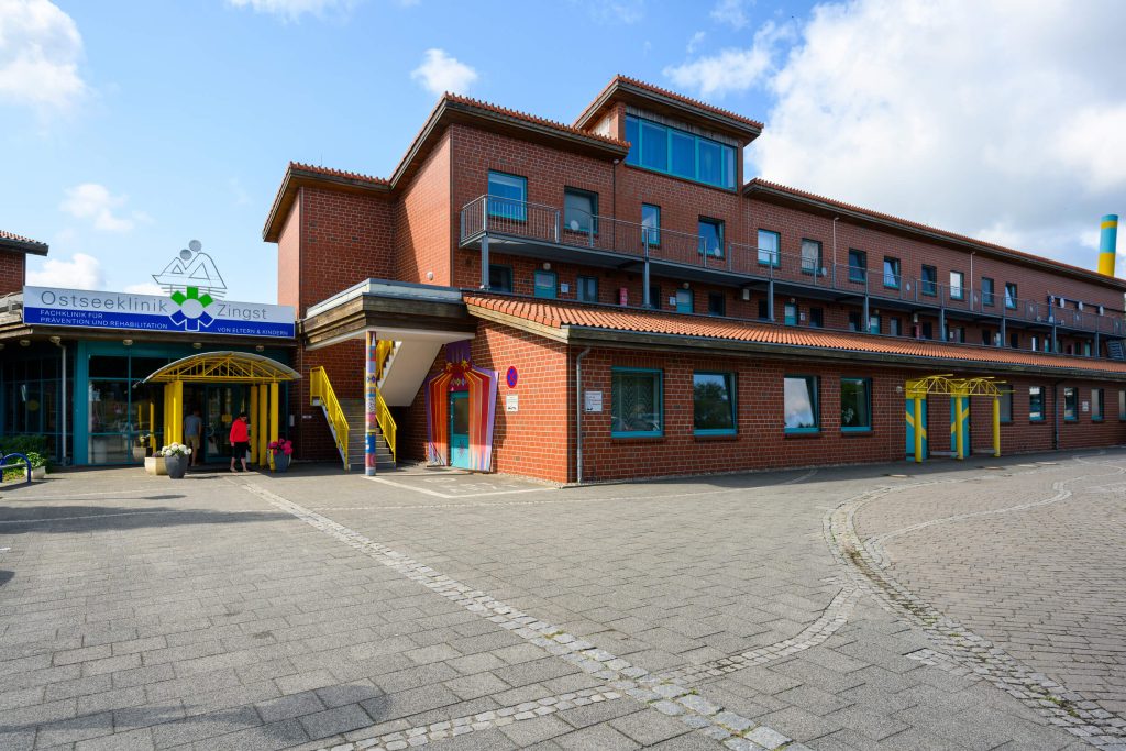 Klinikgebäude der Ostseeklinik Zingst: ein rechteckiger, zweigeschossiger Backsteinbau mit einem Dachaufbau mit Fernster unter blauem Himmel