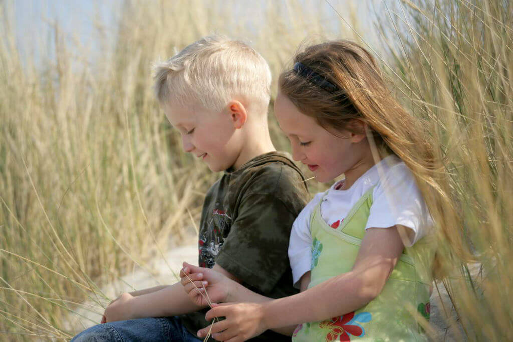 Ein Mädchen und ein Junge sitzen nebeneinander im Dünengras.