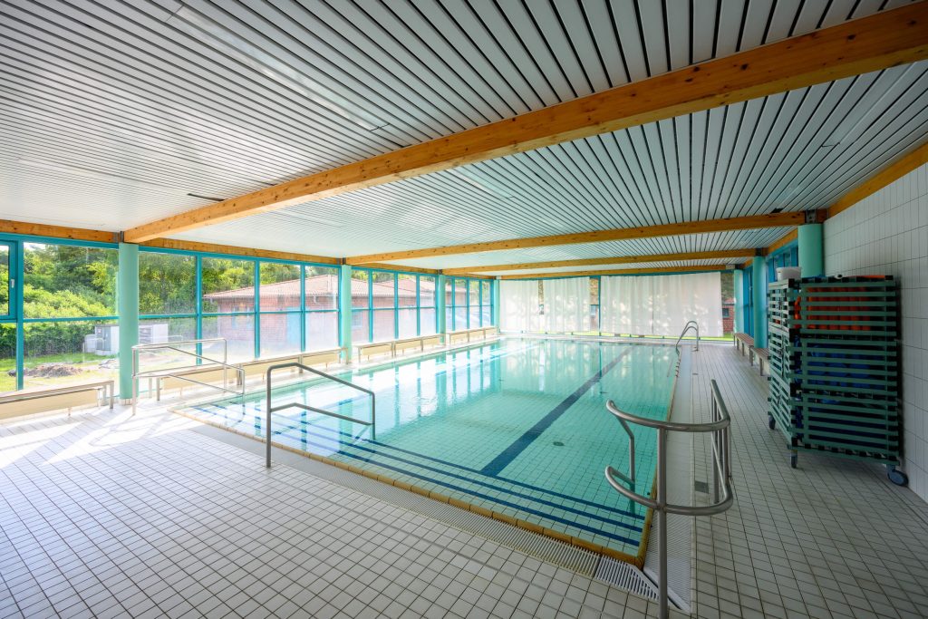 Die lichtdurchflutete Schwimmhalle der Ostseeklinik Zingst, bodentiefe Fenster links und vor Kopf, Schwimmbecken mit Handläufen
