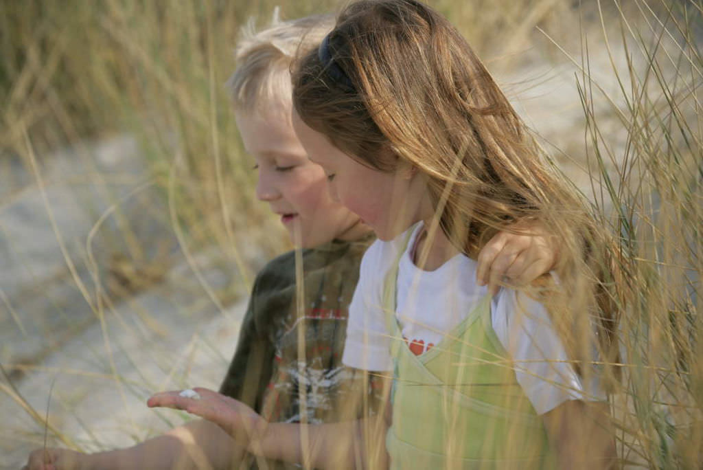 Ein Junge und ein Mädchen sitzen nebeneinander in hohen Dünengräsern.