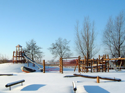 Der schneebedeckte Kinderspielplatz der Ostseeklinik Zingst im Winter unter blauem Himmel.