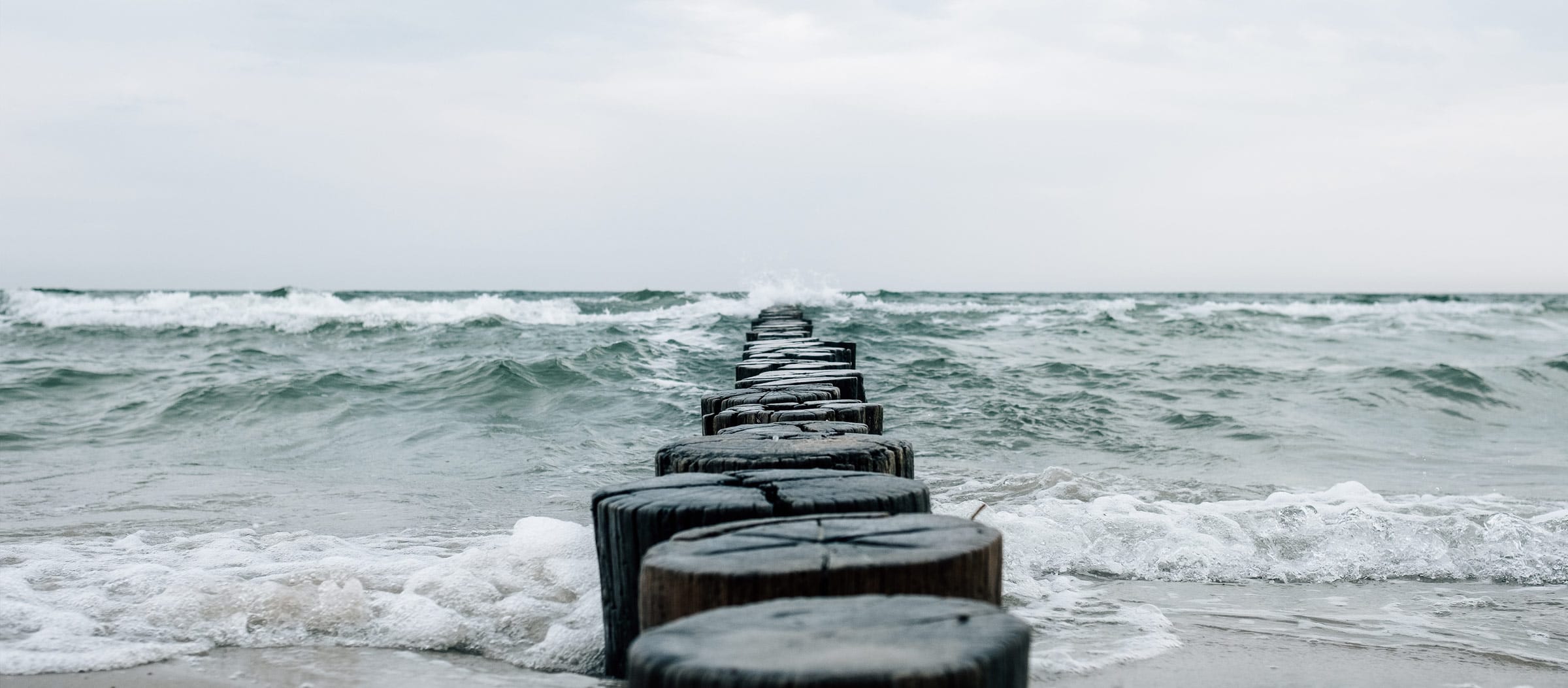Eine Buhne, ein Damm auf Holzpfählen, der sich wie ein Steg in die Ostsee erstreckt.