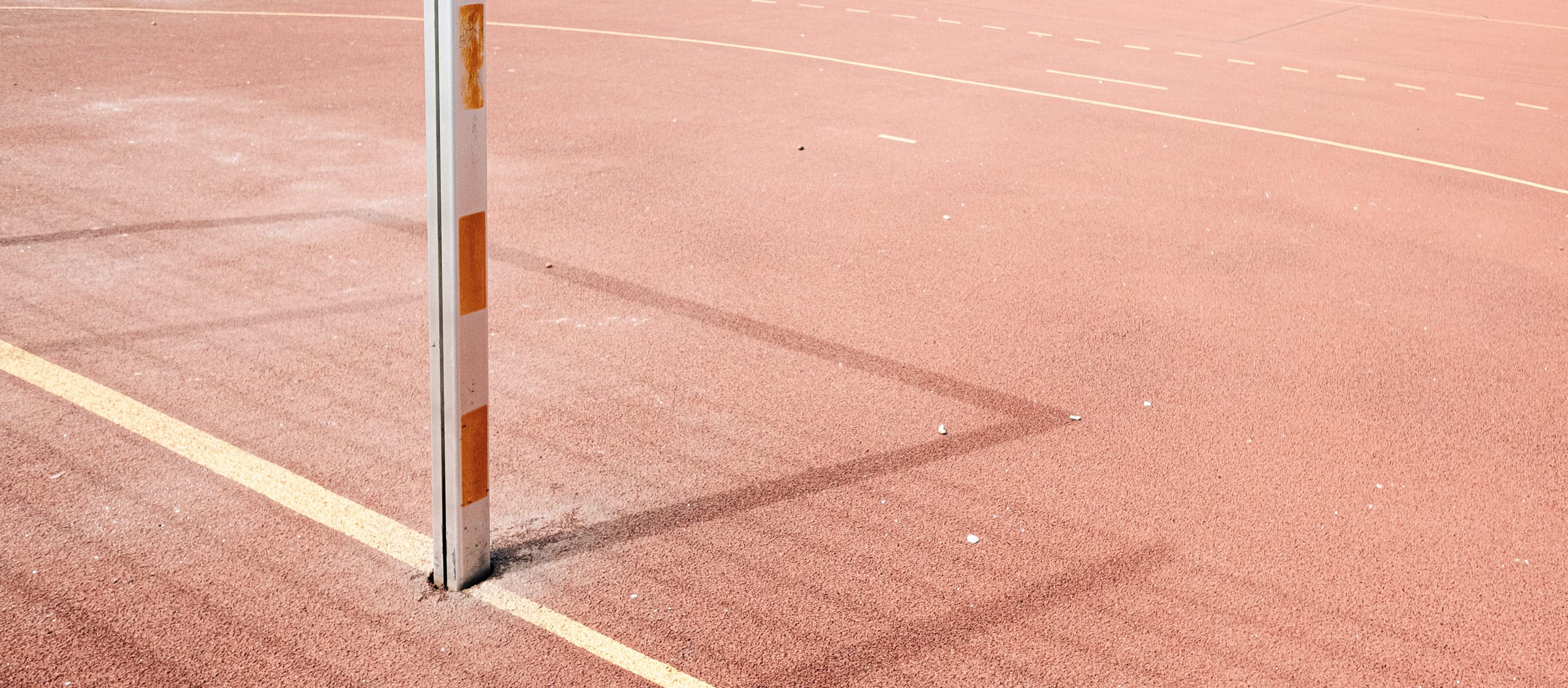 Der Boden eines Sportplatzes mit Ballsportmarkierungen und ein Pfosten eines Tores, das Schatten wirft.