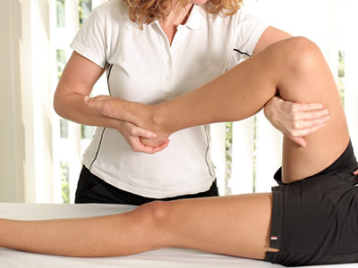 Eine Physiotherapeutin beugt das Bein einer liegenden Patientin.