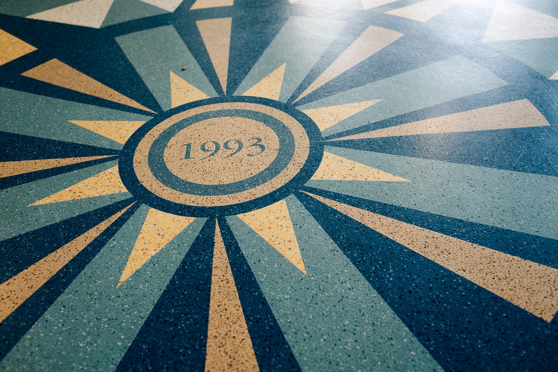 Fußbodengestaltung: die Zahl 1993 innerhalb von zwei Kreisen, von denen sternförmig Strahlen ausgehen. Es erinnert an einen Stern, eine Windrose oder an die Sonne