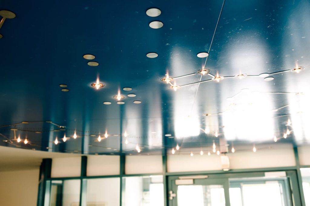 Eine blaue Decke mit eingelassenen Lampen, im Anschnitt ist sind eine Glastüre und ein Fenster zu sehen.