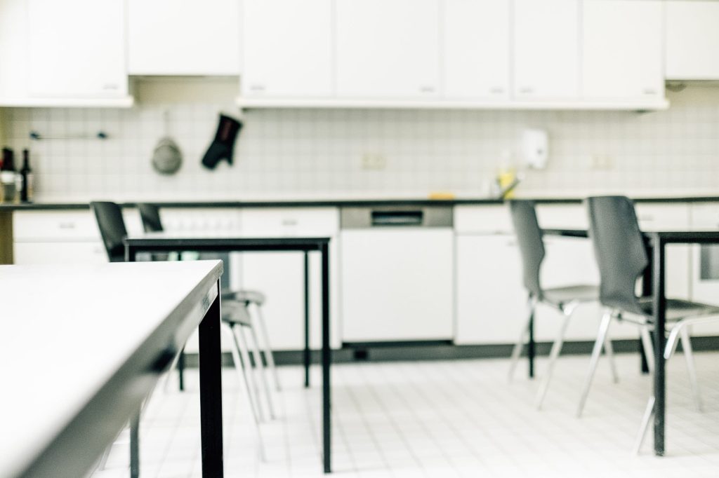 Im Hintergrund eine lange Küchenzeile, davor Tische und Stühle.