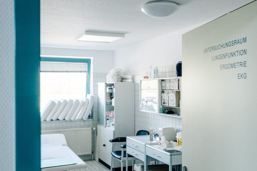Helles Untersuchungszimmer der Klinik, auf der offenen Türe steht Untersuchung, Lungenfunktion, Ergometrie, EKG.