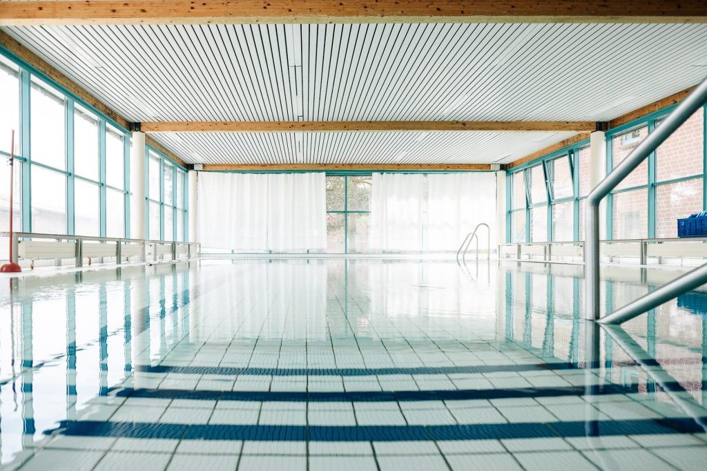 Schwimmbad und Bewegungsbad der Ostseeklinik: in der Mitte das Schwimmbecken mit blauen und weißen Fliesen auf dem Grund des Beckens, rundherum bodentiefe Fenster.