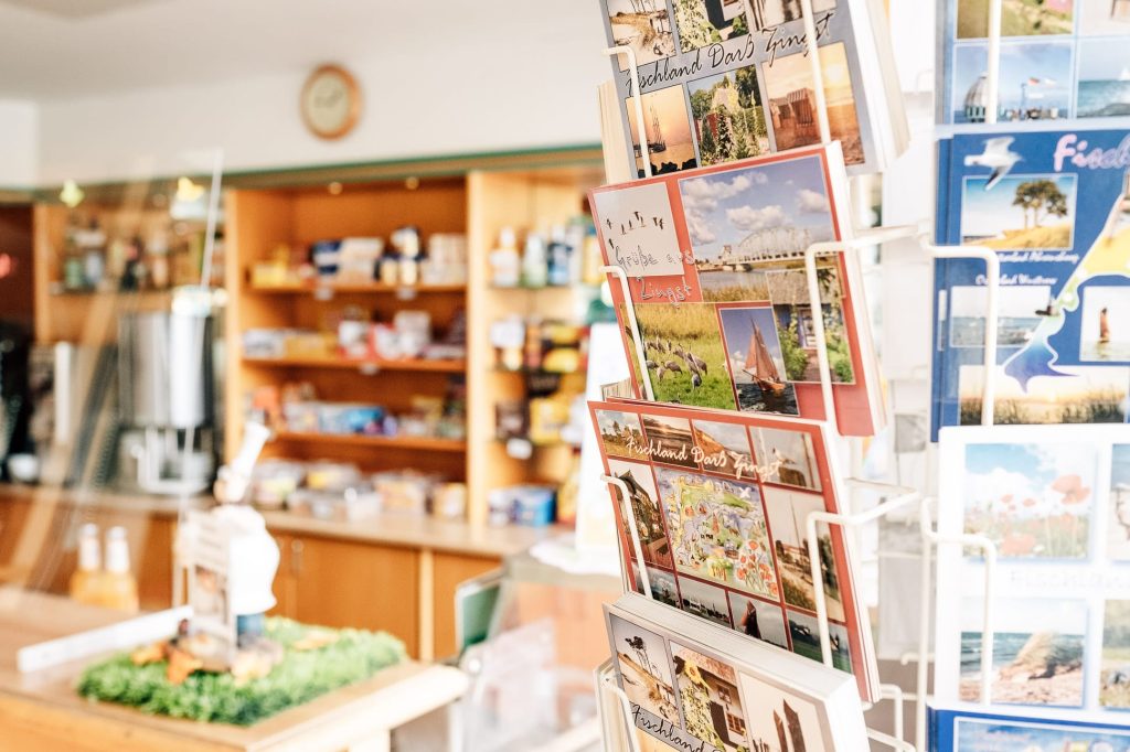 Eingangsbereich der Cafeteria mit Postkartenständer rechts und Holzregalen im Hintergrund.
