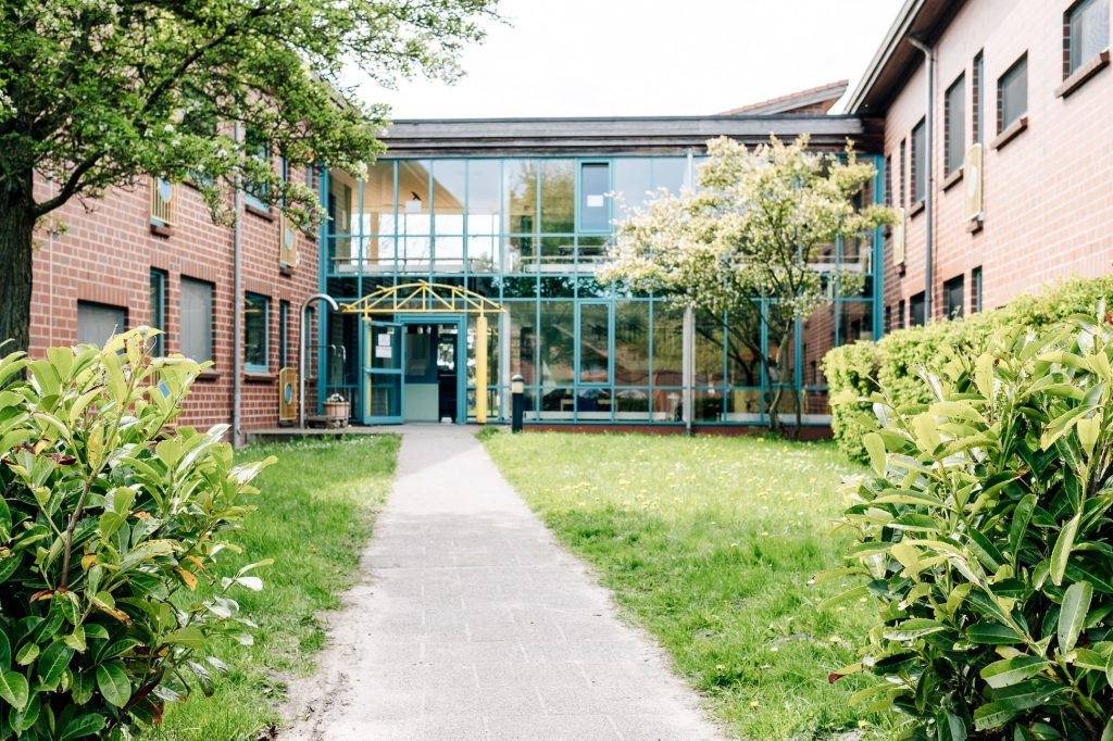 Gebäude der Ostseeklinik mit größer Glasfassade mit Weg davor, der zum Eingang führt.
