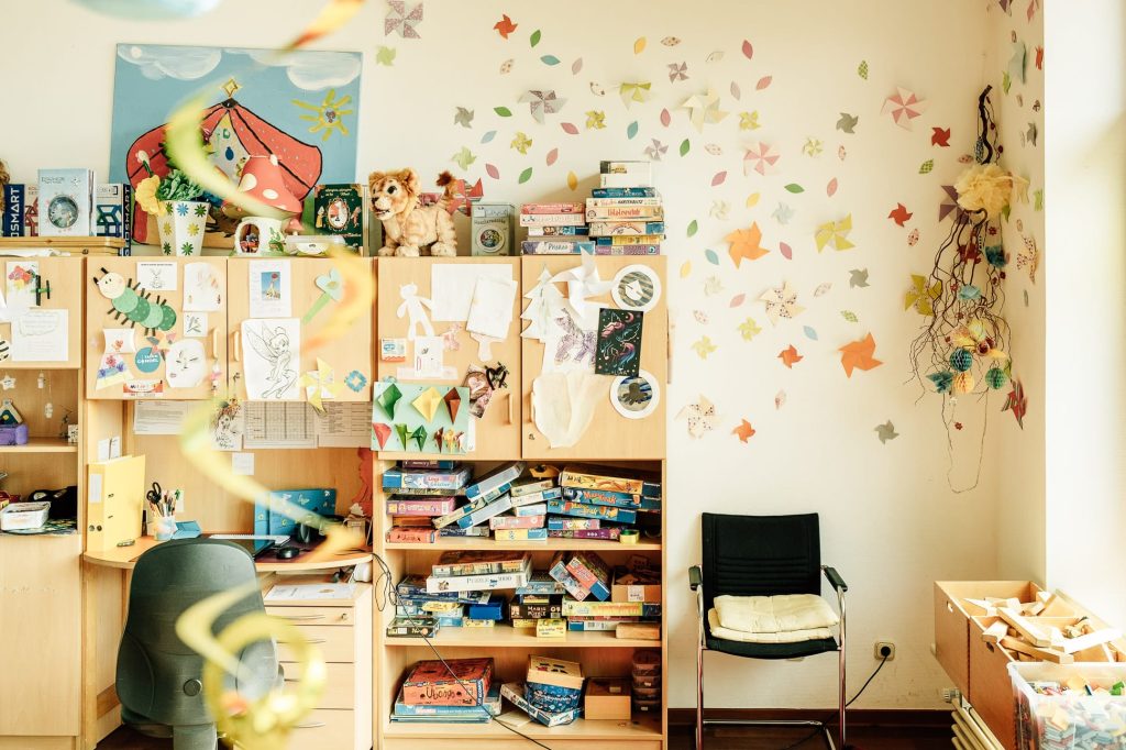 Kindgerecht gestaltetes Spielzimmer: Schränke mit bunten Aufklebern und Zetteln, ein Regal mit Brettspielen.