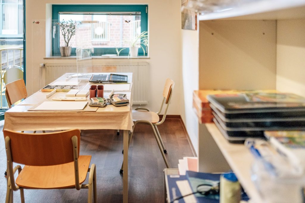 Ein heller Raum mit einem Tisch, auf dem sich Malutensilien befinden.
