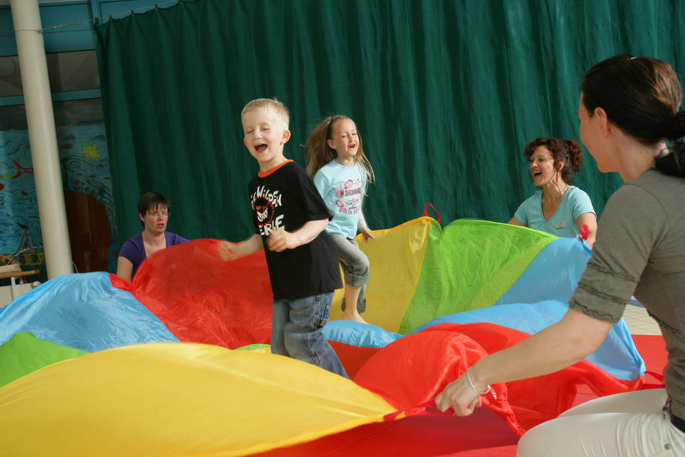 Ein Junge und ein Mädchen hüpfen auf einem bunten Tuch, das von drei Frauen gehalten wird.